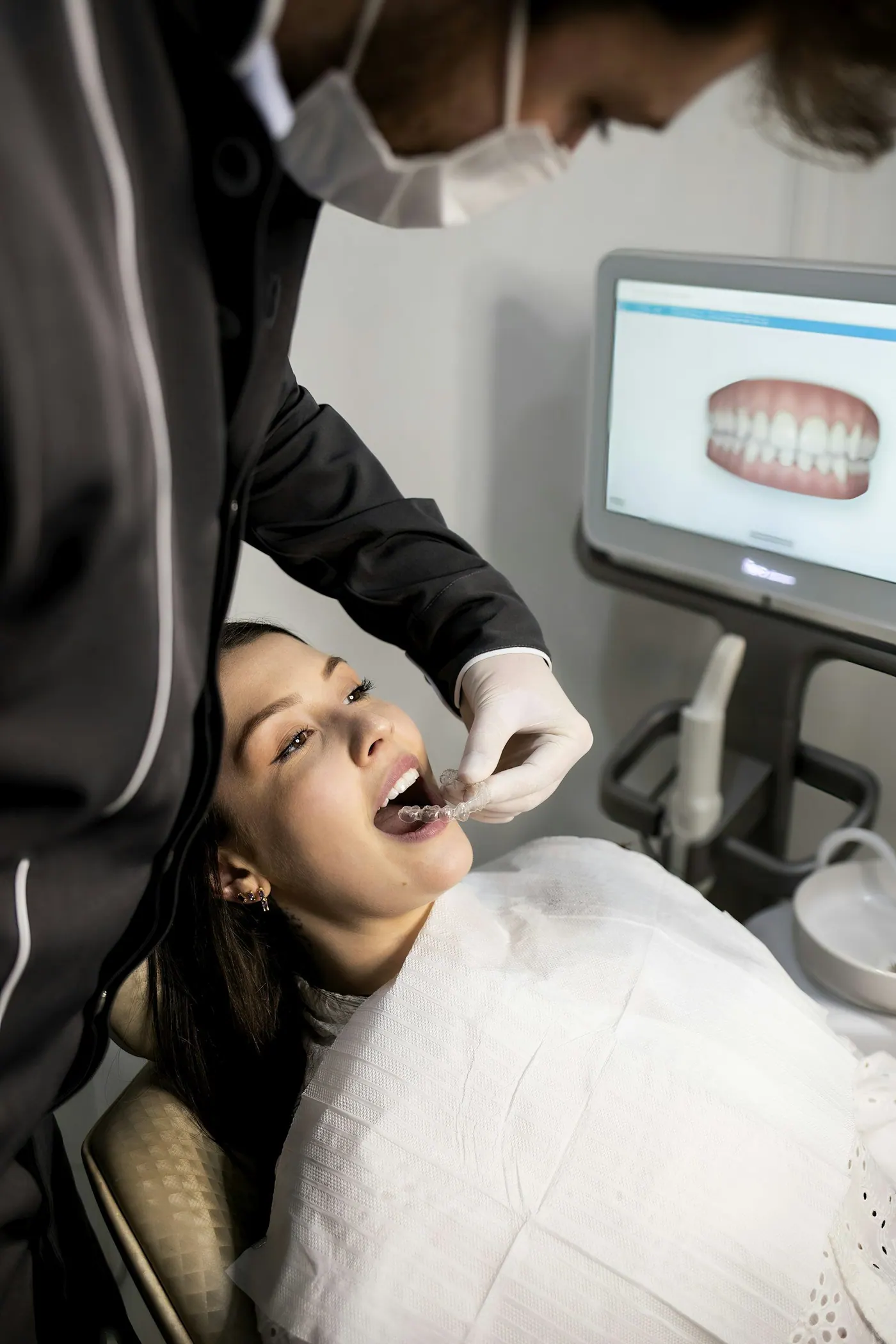 A clinician seating a clear aligner while a three-dimensional scan of the teeth shows on the monitor