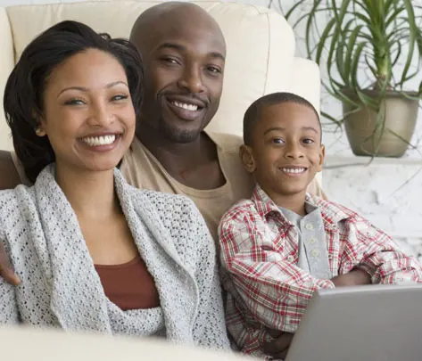 A family of three smiling together on a sofa at home