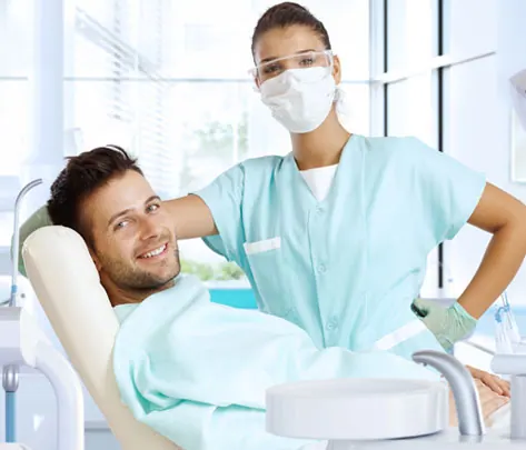 A patient smiling in the chair with a dental professional standing beside him